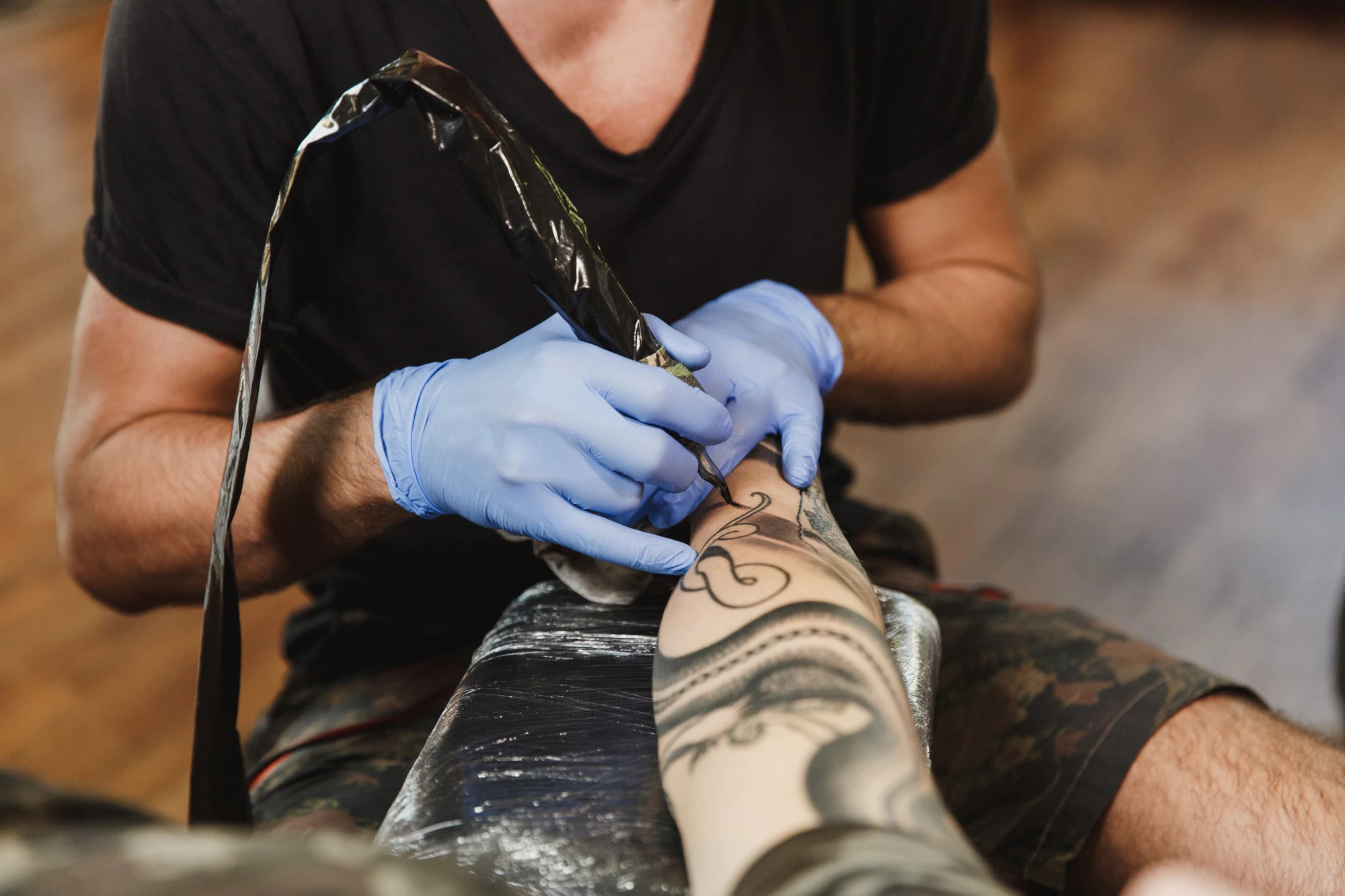 close up of professional tattooer artist doing tattoo on the arm of a young man by machine with black ink 365776 5059