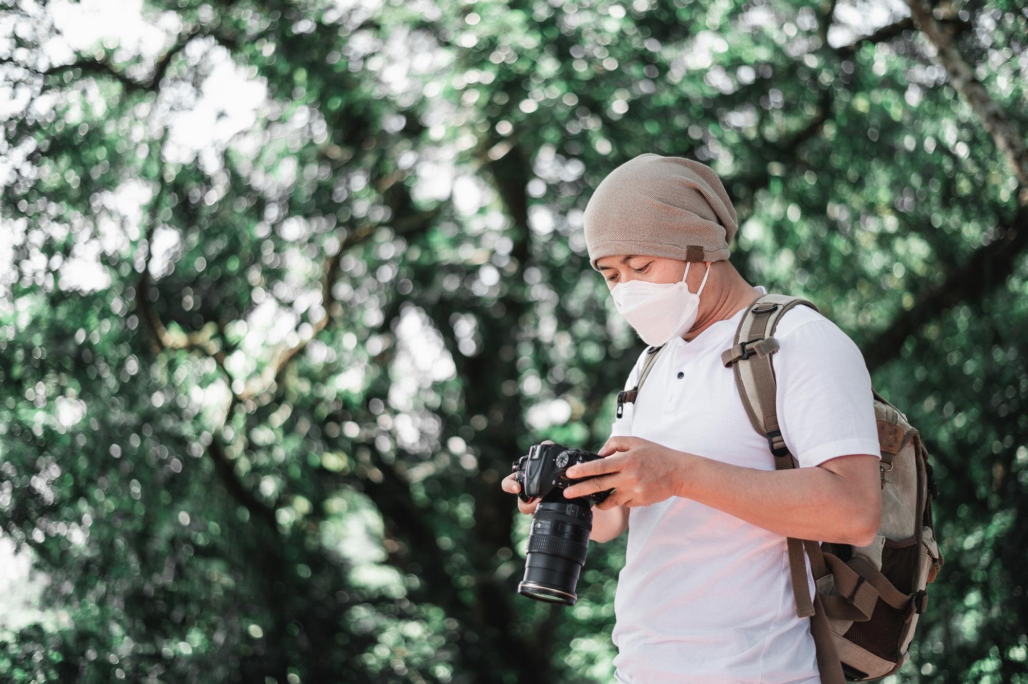 asian traveler man wears medical mask with backpack checking picture camera park with copy space travel photographer vocation holiday concept 1150 61416