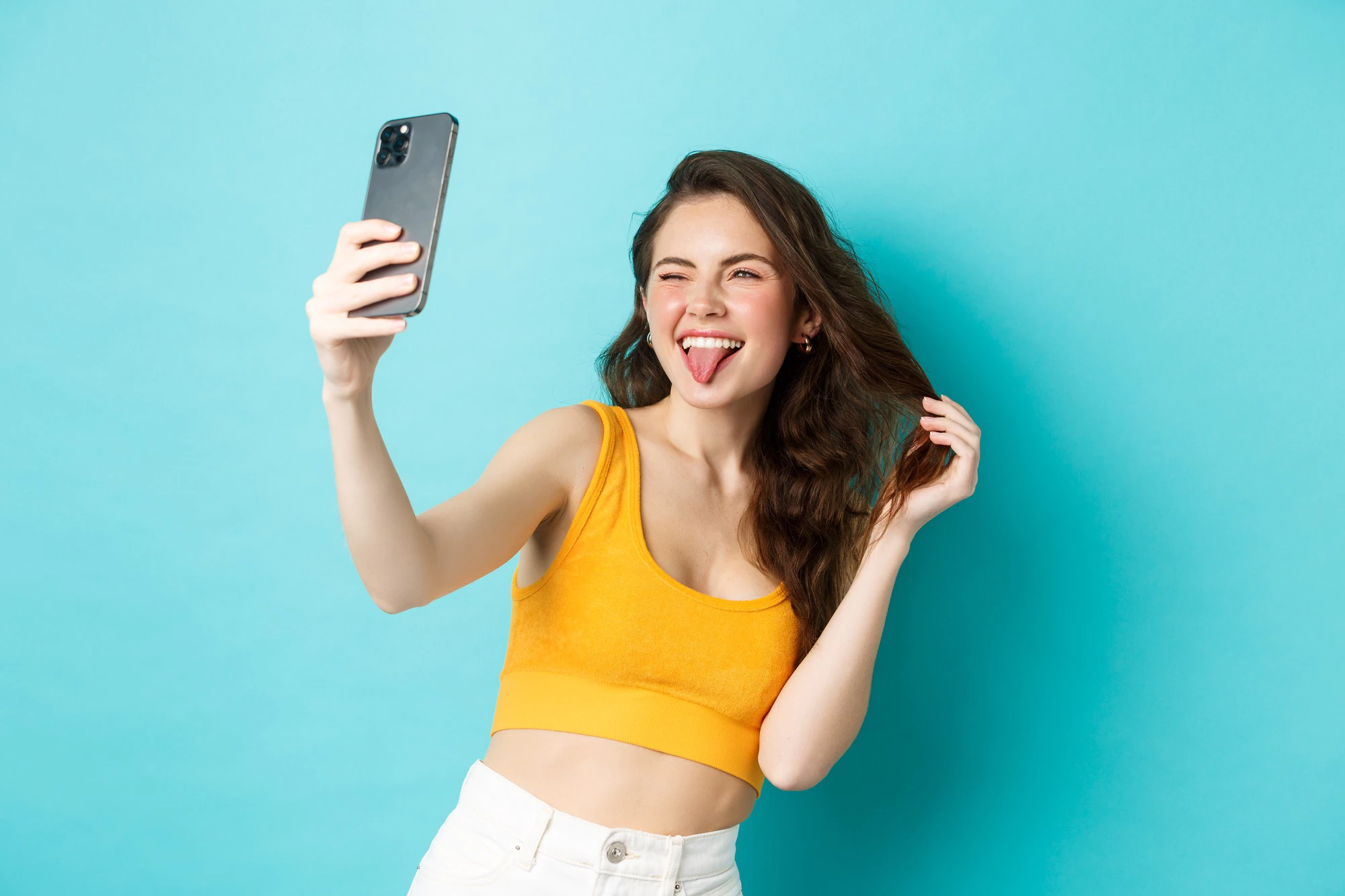 technology lifestyle concept happy young woman making silly faces while taking selfie smartphone app with filters standing against blue background 1258 70390