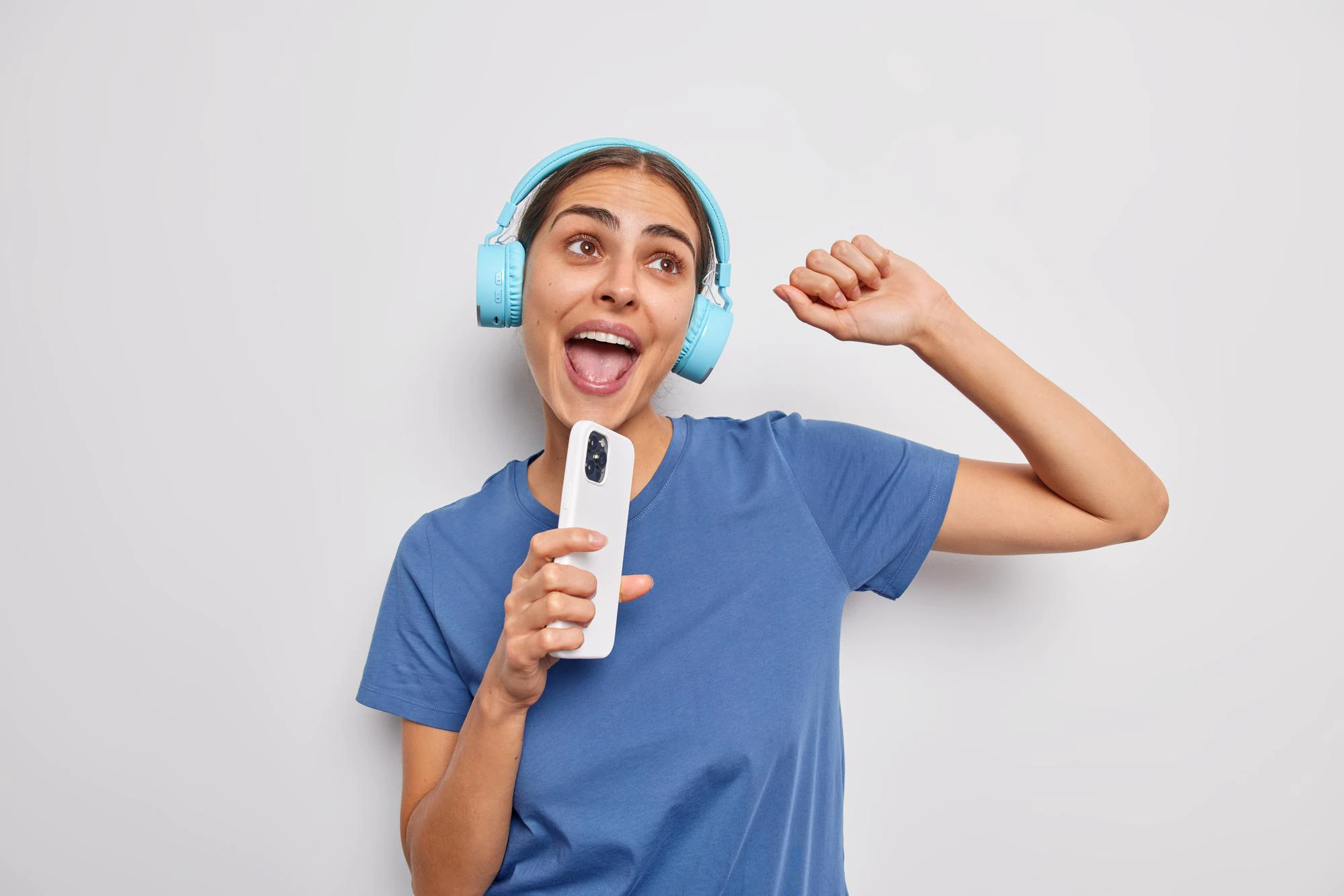 beautiful young european woman dances sing song holds modern smartphone as if microphone uses wireless stereo headphones wears casual t shirt has upbeat mood isolated white background 273609 61049