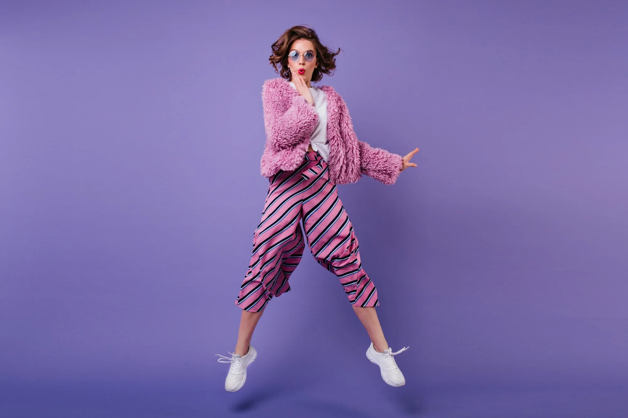 full length shot glad curly woman striped pants jumping purple wall indoor portrait wonderful girl s