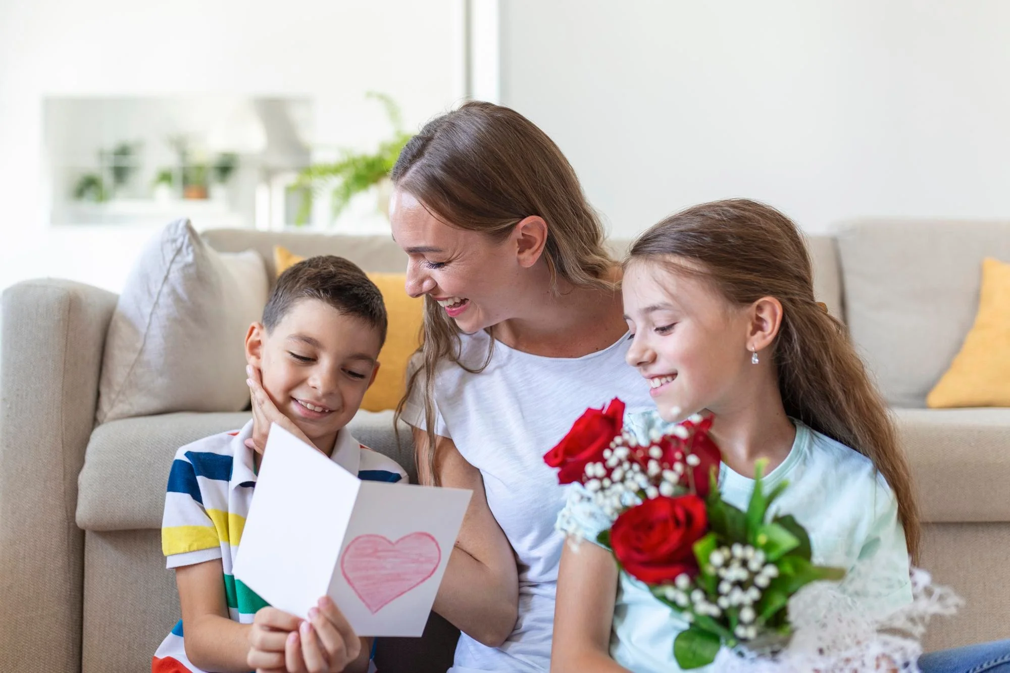 young mother with bouquet roses laughs hugging her son sheerful girl with card congratulates mom during holiday celebration kitchen home 657921 1407